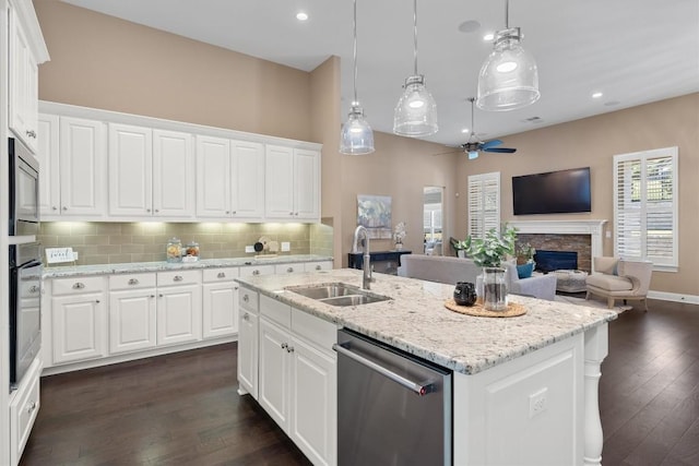 kitchen featuring stainless steel appliances, dark wood-type flooring, sink, white cabinets, and a stone fireplace