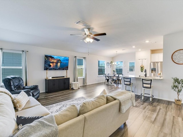 living room with ceiling fan, wood finished floors, visible vents, and baseboards