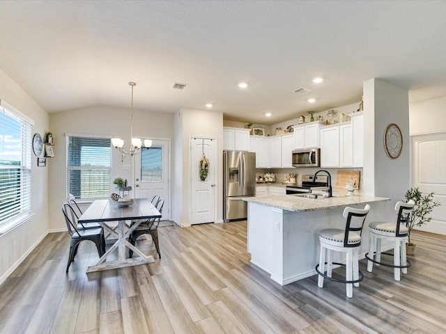 kitchen featuring kitchen peninsula, stainless steel appliances, sink, decorative light fixtures, and lofted ceiling