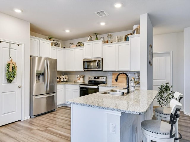 kitchen featuring sink, stainless steel appliances, light stone counters, kitchen peninsula, and white cabinets