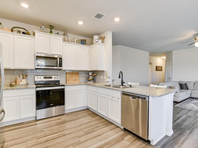 1640 T H Johnson Dr, Taylor, TX 76574 - kitchen with appliances with stainless steel finishes, open floor plan, a peninsula, light wood-style flooring, and white cabinets