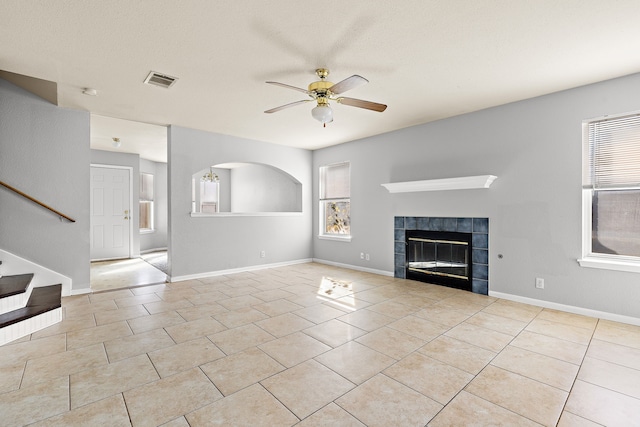 unfurnished living room with a textured ceiling, ceiling fan, light tile patterned flooring, and a fireplace