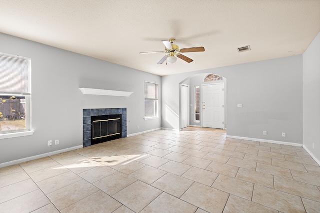 unfurnished living room with ceiling fan, a textured ceiling, light tile patterned floors, and a tiled fireplace