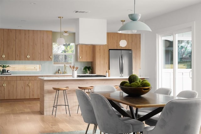 kitchen featuring pendant lighting, tasteful backsplash, light countertops, visible vents, and freestanding refrigerator