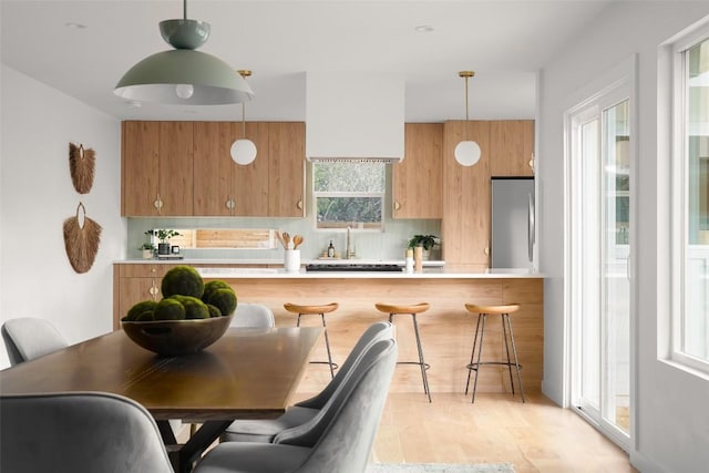 kitchen with a breakfast bar, light countertops, hanging light fixtures, brown cabinets, and stainless steel fridge