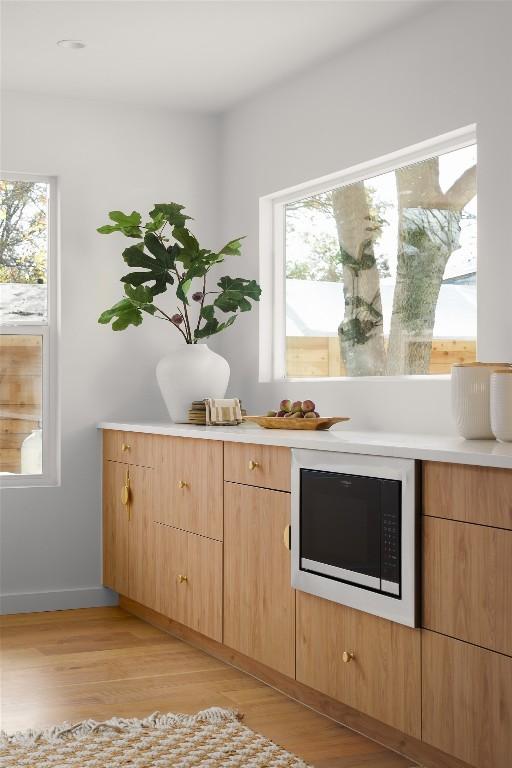 bar featuring built in microwave, light brown cabinets, and light wood-type flooring