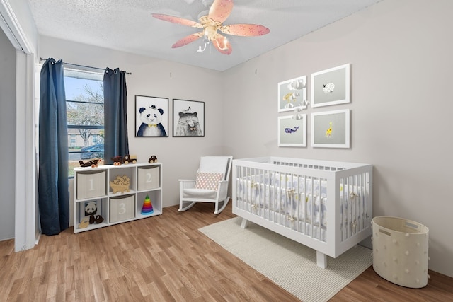 bedroom featuring ceiling fan, wood-type flooring, a crib, and a textured ceiling