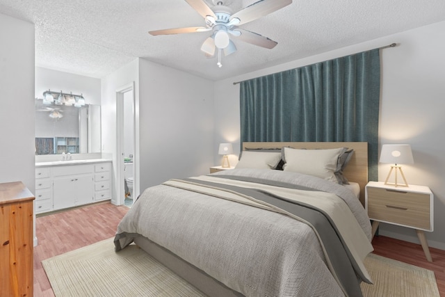 bedroom with ensuite bathroom, a textured ceiling, ceiling fan, sink, and light hardwood / wood-style flooring