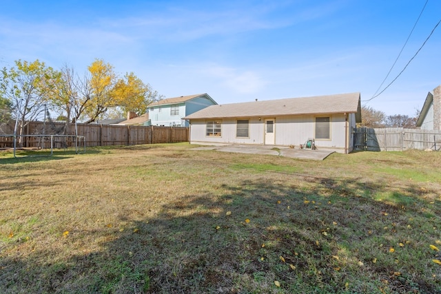 rear view of house featuring a trampoline, a patio area, and a lawn