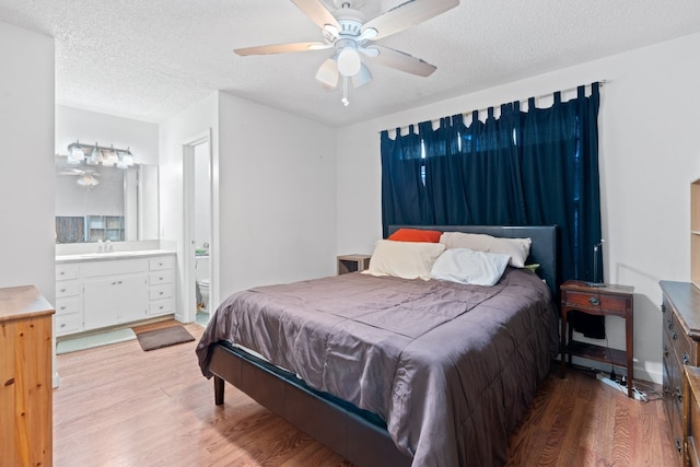 bedroom featuring ensuite bathroom, sink, ceiling fan, light wood-type flooring, and a textured ceiling