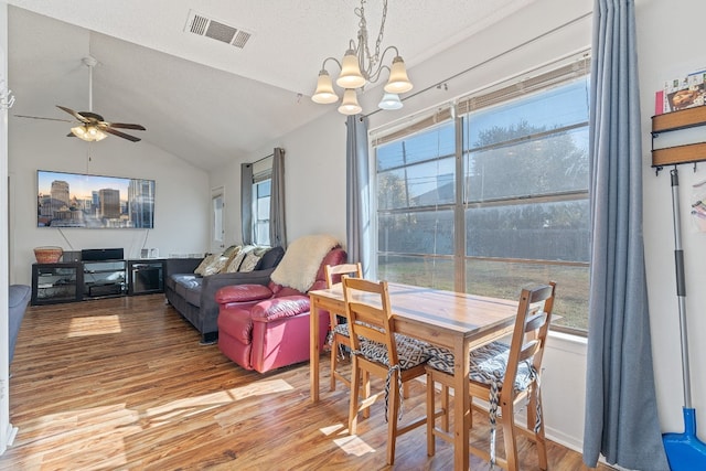 dining room featuring ceiling fan with notable chandelier, light hardwood / wood-style floors, lofted ceiling, and a textured ceiling