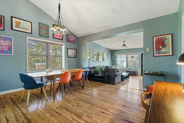 dining room featuring ceiling fan with notable chandelier, light wood-type flooring, a wealth of natural light, and vaulted ceiling