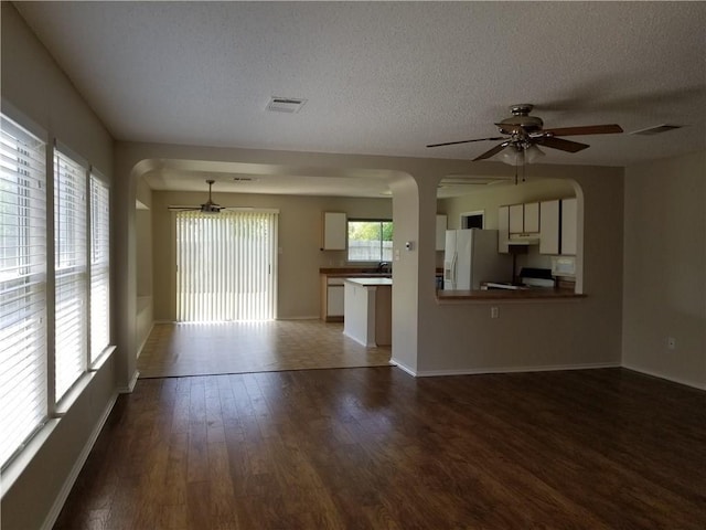 unfurnished living room featuring a textured ceiling, ceiling fan, and dark wood-type flooring