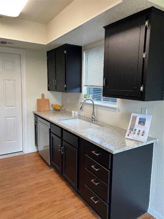 kitchen featuring light stone countertops, sink, stainless steel dishwasher, and light hardwood / wood-style flooring