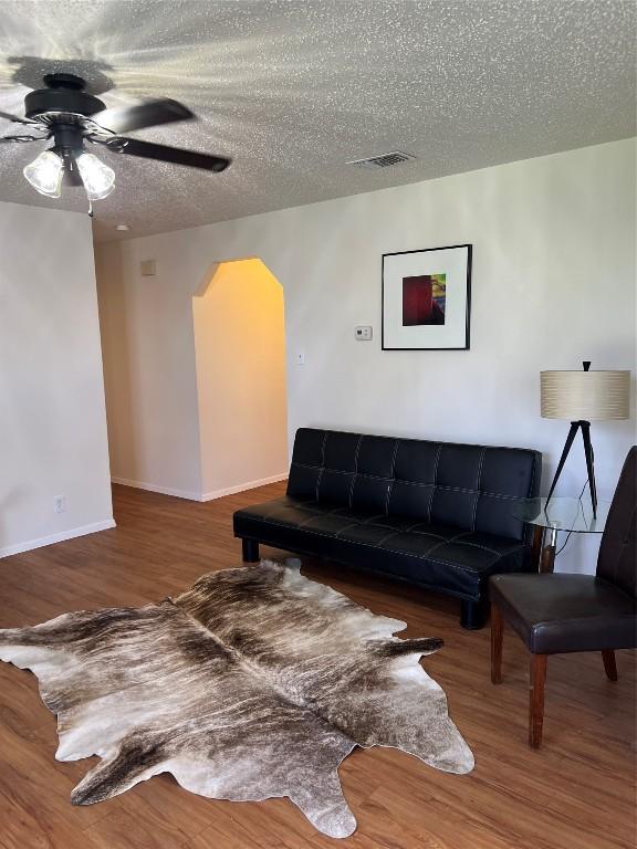 living room featuring wood-type flooring, ceiling fan, and a textured ceiling