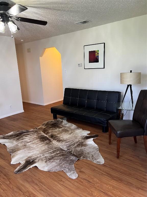 living room featuring wood-type flooring, ceiling fan, and a textured ceiling