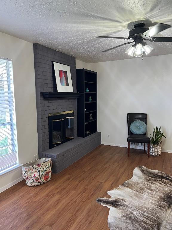 living room with ceiling fan, wood-type flooring, a fireplace, and a textured ceiling