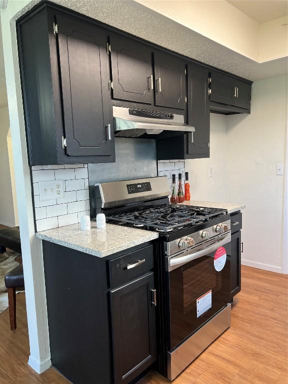 kitchen featuring stainless steel gas range, light wood-type flooring, and decorative backsplash