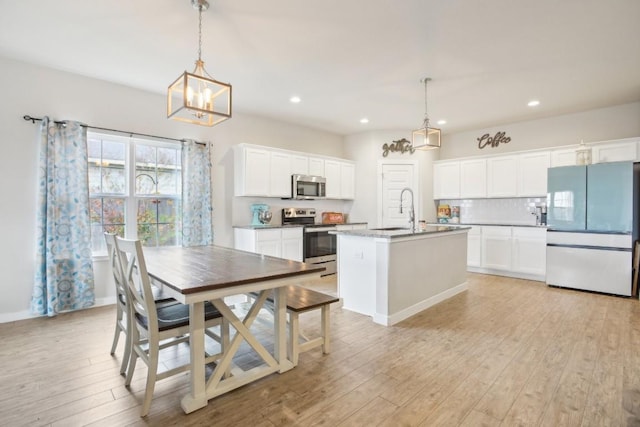 kitchen featuring a kitchen island with sink, white cabinets, light hardwood / wood-style flooring, appliances with stainless steel finishes, and decorative light fixtures