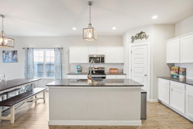 kitchen with a center island with sink, pendant lighting, white cabinets, and stainless steel appliances