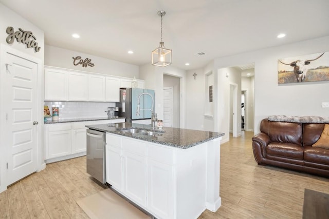 kitchen with stainless steel dishwasher, dark stone counters, light hardwood / wood-style flooring, white cabinetry, and an island with sink