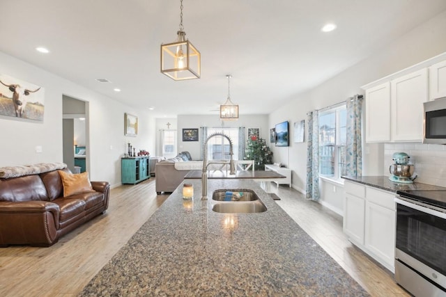 kitchen featuring appliances with stainless steel finishes, light hardwood / wood-style flooring, hanging light fixtures, and dark stone counters