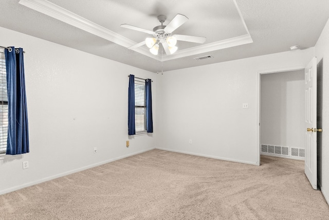 unfurnished room with ceiling fan, a raised ceiling, crown molding, light colored carpet, and a textured ceiling