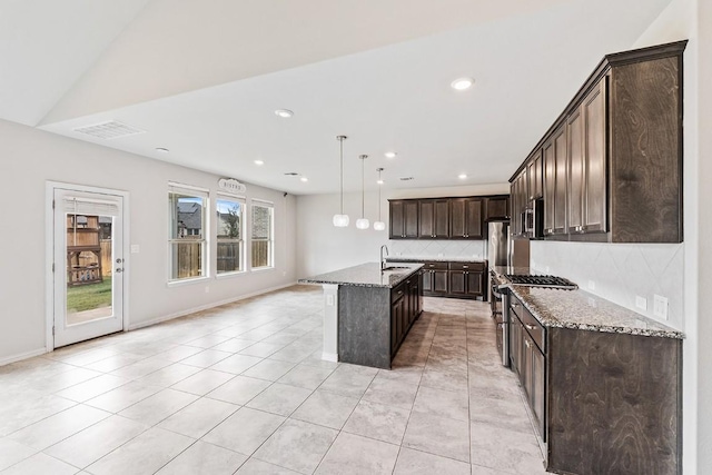 kitchen with lofted ceiling, tasteful backsplash, light stone countertops, an island with sink, and decorative light fixtures