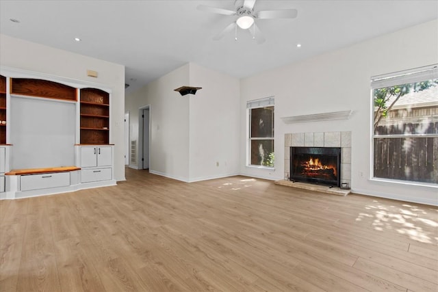 unfurnished living room with a tiled fireplace, ceiling fan, and light hardwood / wood-style flooring