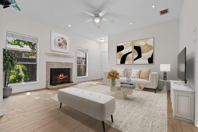 living room with a tile fireplace, ceiling fan, and light hardwood / wood-style flooring