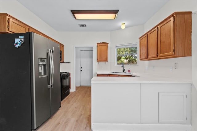 kitchen featuring kitchen peninsula, stainless steel refrigerator with ice dispenser, light wood-type flooring, black range with gas stovetop, and sink