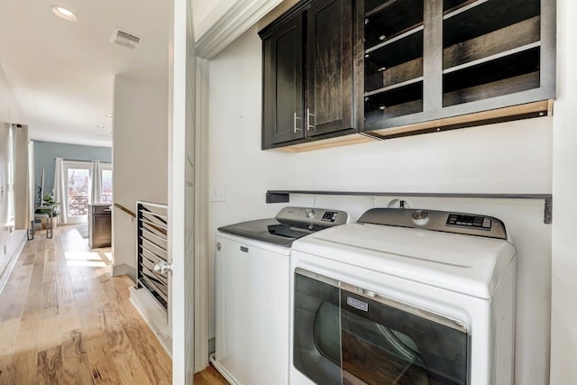 laundry room featuring washer and clothes dryer, light hardwood / wood-style floors, and cabinets