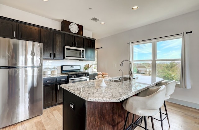 kitchen with light hardwood / wood-style flooring, sink, stainless steel appliances, and an island with sink