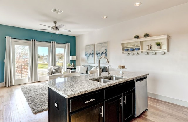 kitchen featuring light stone countertops, sink, light hardwood / wood-style flooring, stainless steel dishwasher, and a kitchen island with sink