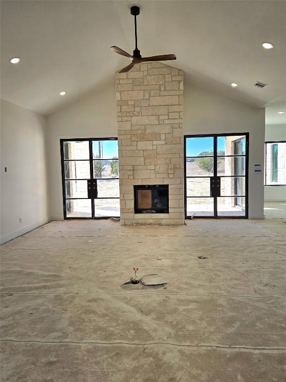 unfurnished living room with concrete flooring, high vaulted ceiling, a stone fireplace, and ceiling fan