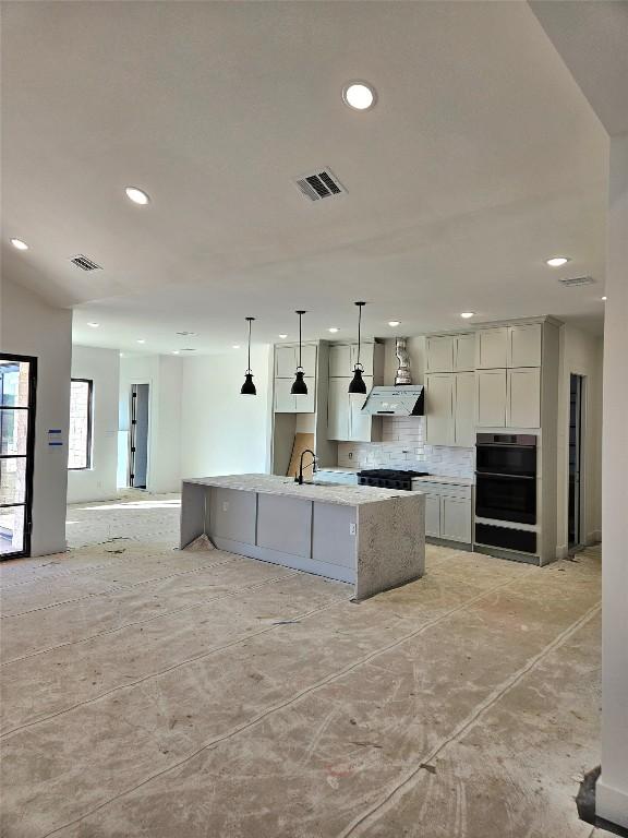 kitchen with hanging light fixtures, decorative backsplash, light stone countertops, double oven, and a large island