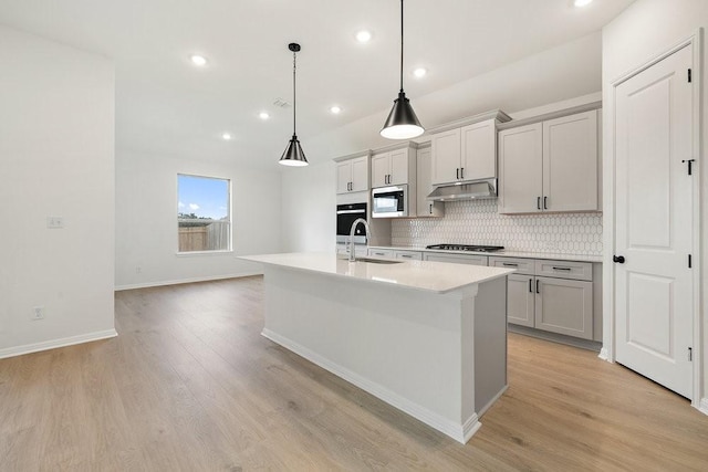 kitchen with a kitchen island with sink, hanging light fixtures, gray cabinets, light wood-type flooring, and appliances with stainless steel finishes