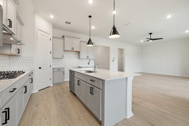 kitchen featuring appliances with stainless steel finishes, ceiling fan, sink, light hardwood / wood-style floors, and an island with sink