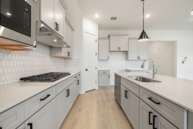 kitchen featuring pendant lighting, sink, light wood-type flooring, light stone counters, and stainless steel appliances