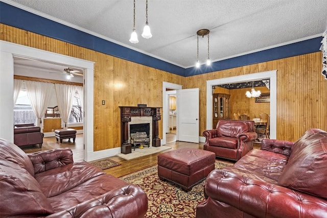 living room with ceiling fan with notable chandelier, a textured ceiling, hardwood / wood-style flooring, and ornamental molding