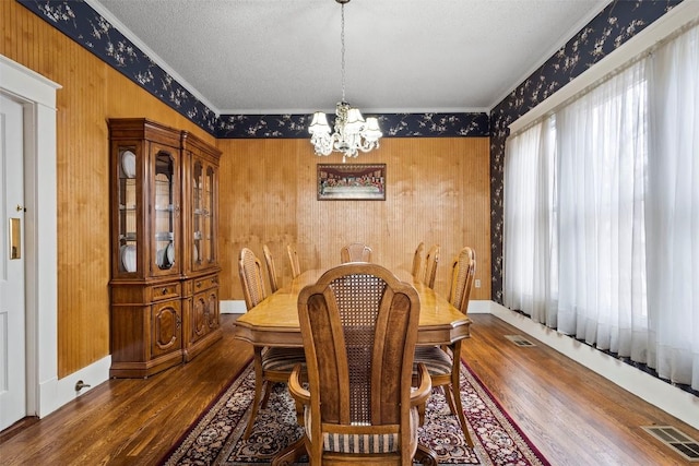 dining space featuring crown molding, wooden walls, a textured ceiling, a notable chandelier, and wood-type flooring