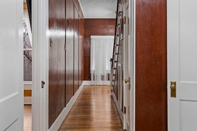 hallway featuring wood-type flooring, a textured ceiling, and wood walls