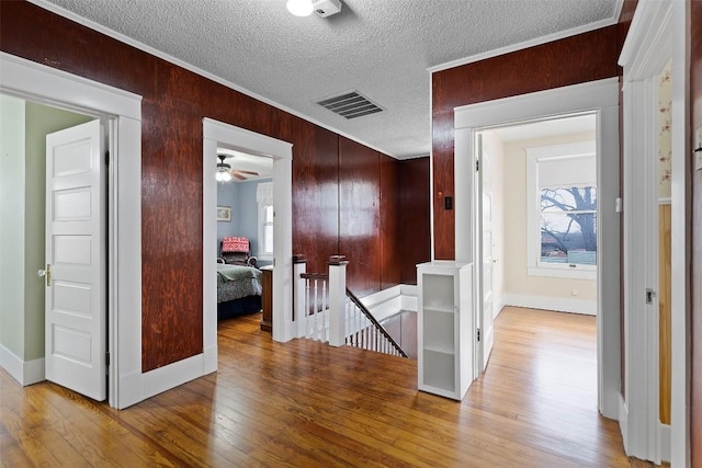 corridor with wooden walls, light hardwood / wood-style floors, a textured ceiling, and ornamental molding