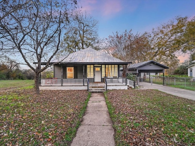 bungalow-style home with concrete driveway, a detached carport, metal roof, fence, and covered porch