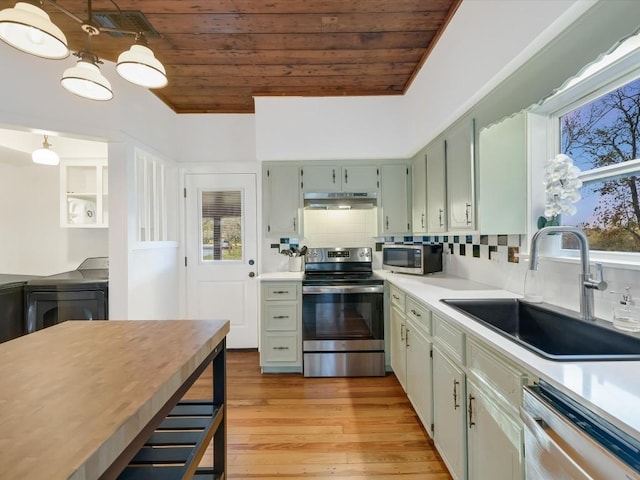 kitchen featuring under cabinet range hood, washer / dryer, appliances with stainless steel finishes, wood ceiling, and a sink
