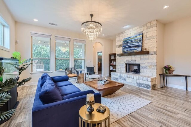 living room with light hardwood / wood-style floors, a stone fireplace, a wealth of natural light, and a chandelier