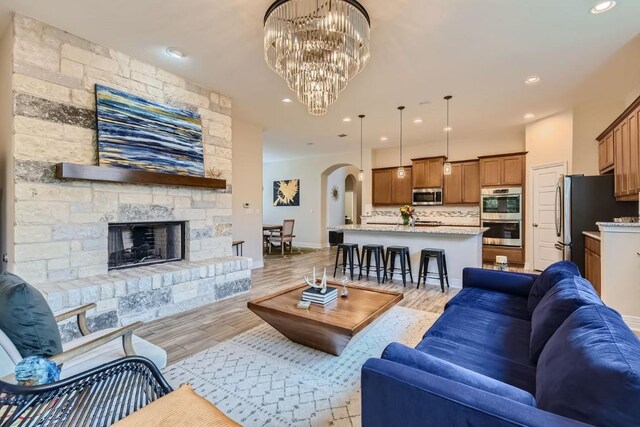 living room featuring light hardwood / wood-style floors, a stone fireplace, and a chandelier