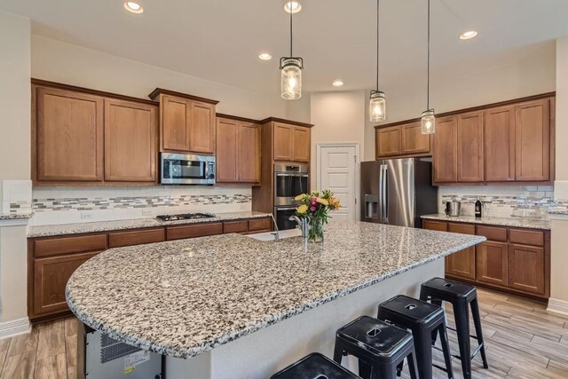 kitchen featuring decorative backsplash, light stone countertops, light wood-type flooring, decorative light fixtures, and stainless steel appliances