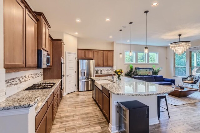 kitchen featuring a chandelier, a spacious island, decorative light fixtures, appliances with stainless steel finishes, and light wood-type flooring