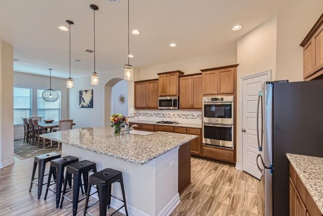 kitchen with hanging light fixtures, an island with sink, a breakfast bar, appliances with stainless steel finishes, and light wood-type flooring